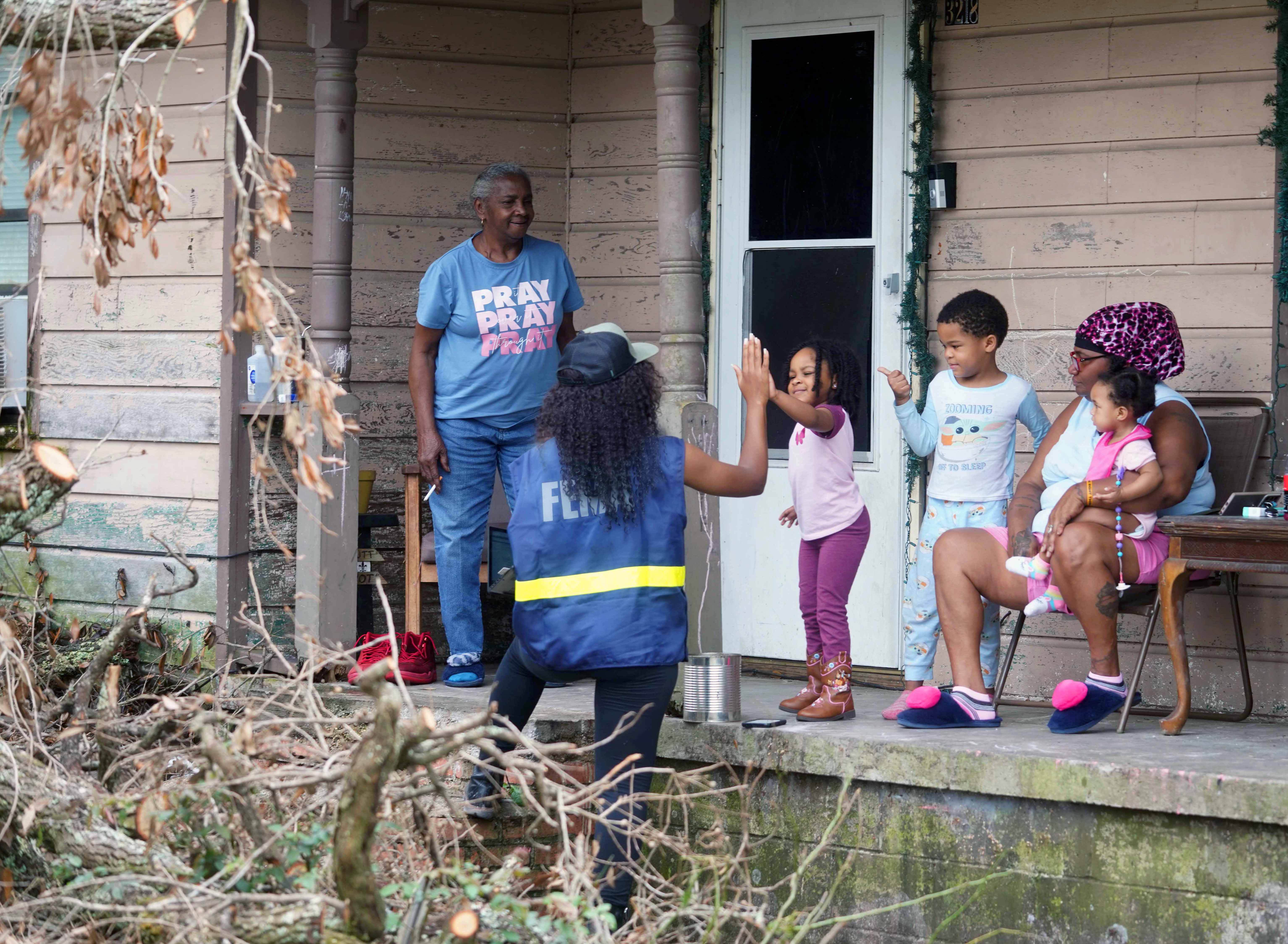 A woman in a FEMA vest talks to children and adults on a front porch