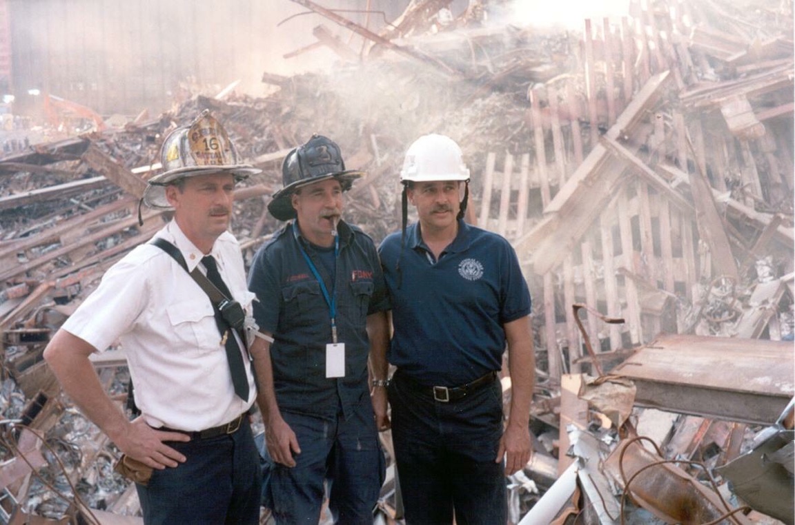Fred Endrikat and two other responders wearing helmets in front of building debris