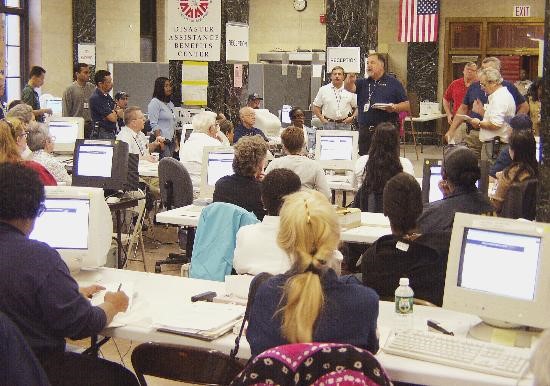 FEMA employees sitting in front of computers listening to a man in a blue shirt speak